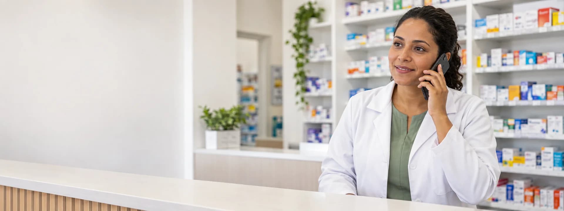 Imagem ilustrativa de uma farmacêutica de jaleco atendendo por telefone em uma farmácia.